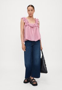 Rosa uten ermer topp med volanger, paret med vide mørkeblå jeans. Svart tote bag og chunky sandaler med naglede detaljer.