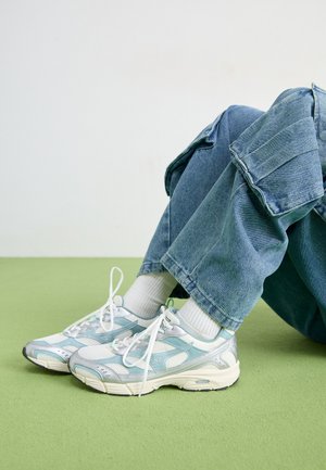 Lichtblauwe sport sneakers met witte netstof, rubberen zool en zilveren accenten, gecombineerd met opgerolde spijkerbroek en witte sokken.