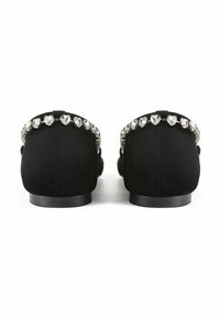 Zapatos negros de ante tipo slip-on con una fila de acentos de brillantes en forma de corazón a lo largo de la parte de atrás, con una suela plana de goma.