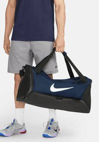 Bolsa de deporte azul marino con acentos negros y un logo de Nike blanco, que cuenta con asas dobles y un compartimento con cremallera. Tejido texturizado.