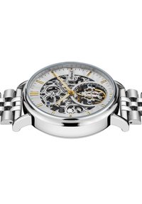 Montre en acier inoxydable argenté avec un cadran squelette, des aiguilles et des marqueurs d'heure dorés, présentant des motifs découpés complexes et un bracelet en maille.