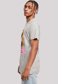 Graues Baumwoll-T-Shirt mit kurzen Ärmeln, das ein lebhaftes Grafikdruck auf der Vorderseite zeigt. Das Design umfasst fetten pinken Text und ein farbenfrohes Bild.
