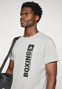 Grå bomull T-skjorte med svart vertikal tekst "BOXING" og Adidas-logo. Rund hals, kort erme og myk tekstur.