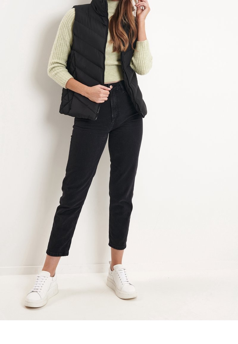 Černá prošívaná vesta přes světle zelený žebrovaný rolák, spárovaná s černými džínami s vysokým pasem a bílými teniskami. Jednoduchý design a střih.
