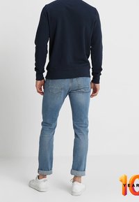 Sudadera azul oscuro de manga larga, combinada con vaqueros azul claro. Los vaqueros están remangados en los puños, y unas zapatillas blancas completan el conjunto.