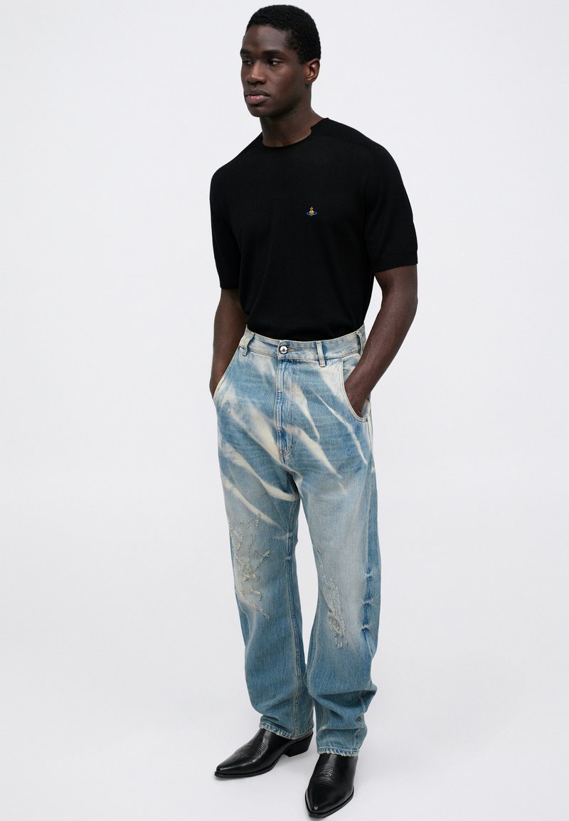 Svart kortärmad tröja, ljusblå slitna jeans med vita streck och svarta spetsiga ankelskor. Tygernas texturer synliga.