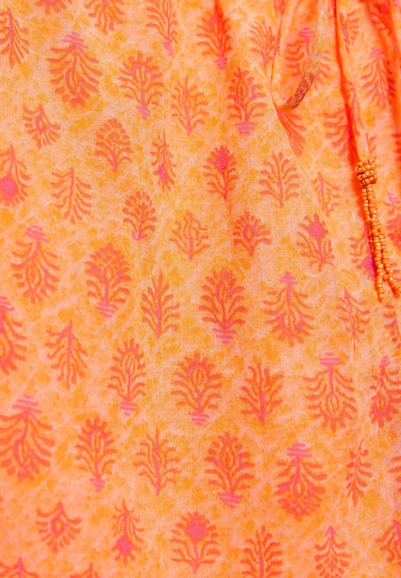 Tissu orange avec un motif floral répété en rouge et rose, montrant un cordon avec de petites perles orange sur le côté.
