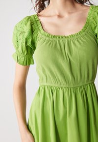 Grünes Kleid mit einem strukturierten Oberteil, das über Rippdetails verfügt, und bestickten Puffärmeln. Der Rock ist an der Taille gerafft für einen fließenden Sitz.