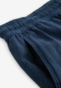 Mørkeblå bukser med elastisk talje, struktureret stof og plisserede detaljer ved taljen. Fokus på Komfort og pasform.