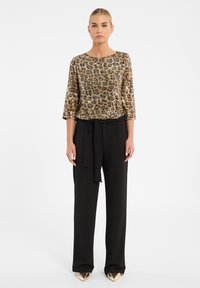 Haut à sequins dorés et noirs avec des manches trois-quarts, associé à un pantalon noir taille haute avec une ceinture nouée. Chaussures dorées à bout pointu.