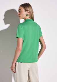 Grön polo skjorta i bomull med klassisk krage, korta ärmar och lätt textur. Bärs med beige byxor som visar en modern passform.