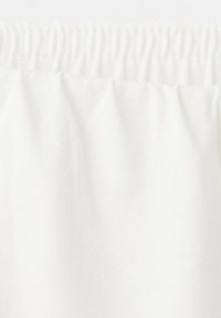 White fabric with elasticated waistband, showing texture and gathered detail on lightweight material.