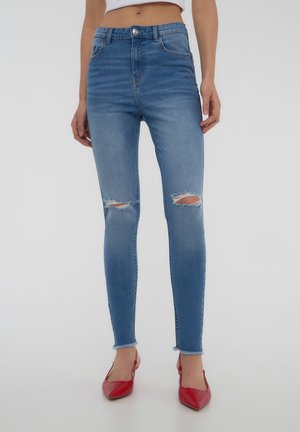 Jeans skinny in denim azzurro chiaro con fori strappati alle ginocchia e orlo grezzo. Abbinati a scarpe rosse con punta a punta.