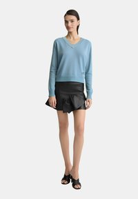 Maglione lavorato a maglia azzurro chiaro con scollatura a V e orlo a coste, abbinato a una mini gonna in pelle nera con dettagli arricciati e scarpe nere con punta aperta.