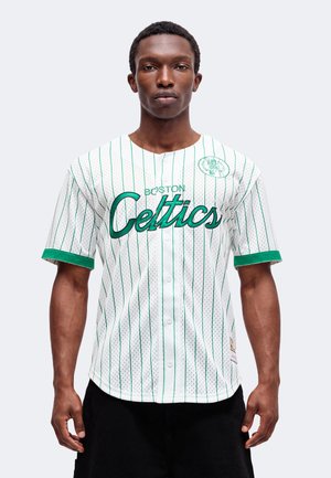 Homme portant un maillot blanc des Boston Celtics avec des rayures verticales vertes et des bordures vertes aux manches sur un fond clair uni.