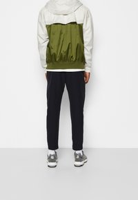 Giacca da uomo con parte superiore bianca e parte inferiore verde oliva, vita elastica, abbinata a pantaloni neri aderenti e sneakers grigie.