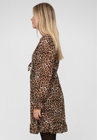 Kleid mit Leopardenmuster, langen Ärmeln, gerafftem Saum und Bindegürtel in der Taille. Hergestellt aus leichtem, durchscheinendem Stoff in braunen und sandfarbenen Tönen.