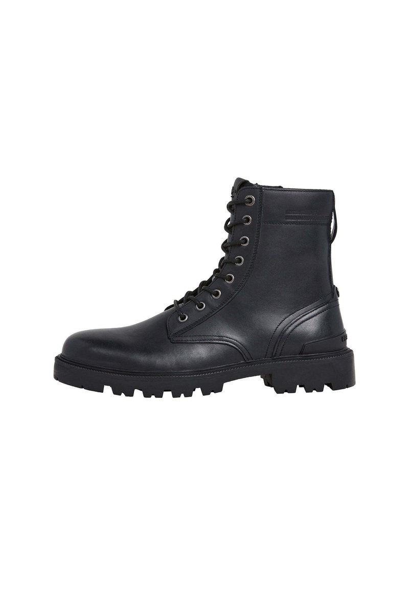 Botas de tobillo de cuero negro con punta redonda, cordones frontales y suela con tacos para mayor tracción. Presentan ojales de metal y una tirador.