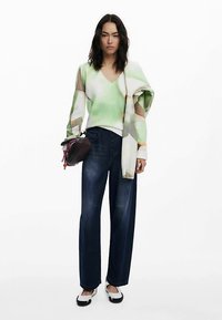 Valgest ja beežist geomeetrilise mustriga kampsun, kombineeritud tumesiniste laiade pükstega. Aksessuaar: väike tumedat värvi kott. Mustad ja valged jalanõud.