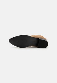 Scarpa in suede beige con un design tessuto e stratificato e punta affusolata. La suola in gomma nera presenta una texture a righe per una migliore aderenza.