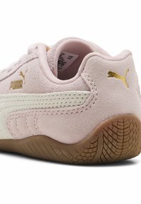 Zapatillas de ante rosas con una franja lateral blanca y acentos dorados en el logotipo. Presenta una suela de goma texturizada para mayor tracción.
