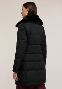 Czarna puchowa kurtka z kołnierzem z sztucznego futra. Ma pikowane sekcje i długie rękawy. Widok z tyłu pokazuje gładką fakturę i zorganizowany krój.