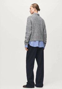 Szary dziergany sweter z wysokim kołnierzem, prążkowaną teksturą i długimi rękawami, noszony na niebiesko-białej paskowanej koszuli oraz ciemnych spodniach.