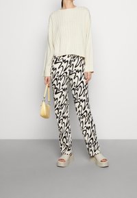 Maglione a coste crema, pantaloni a righe ondulate bianco e nero, sandali con plateau grigi e una piccola borsa gialla.