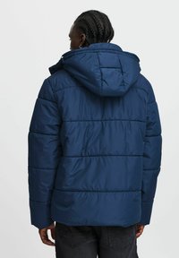 Marinblå vadderad jacka med huva, med horisontell sömnad, en slät textur och en något förlängd bakslut.