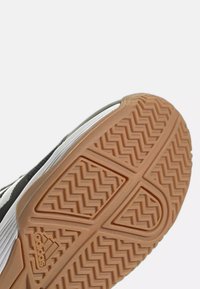 Semelle d'une chaussure Adidas noire et blanche avec une bande de roulement en caoutchouc brun à motif en zigzag et logo Adidas.