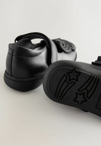 Czarne skórzane buty z okrągłym noskiem i paskiem na rzep. Podeszwa ma wzór gwiazdy i fal dla lepszej przyczepności.