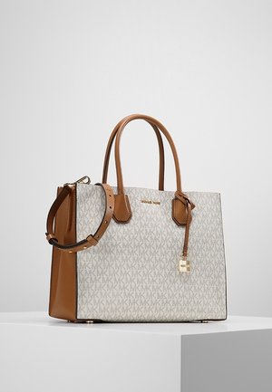 Cream and brown Michael Kors handbag with double handles, adjustable shoulder strap, and gold-tone lock charm on a white surface.