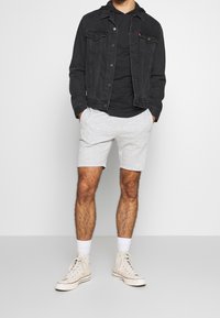 Černá džínová bunda přes černé tričko, šedé sportovní šortky a béžové vysoce uřezané tenisky s bílými ponožkami. Jednoduchý, neform�ální outfit.