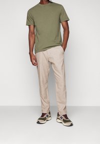 Olive green T-shirt, beige textured trousers, and multi-colored sneakers with prominent logo and accents. Simple and casual design.