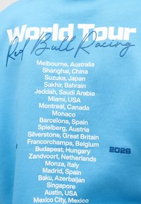 Tela azul con el texto "World Tour Red Bull Racing" y una lista de ubicaciones internacionales de carreras para 2026, incluyendo Melbourne, Mónaco y Austin.