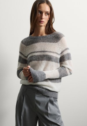 Pull rayé dans des tons crème, gris et gris clair, avec un col rond et des poignets côtelés. Associé à un pantalon gris, ajusté.