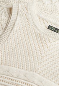 Cremfarbener, gestrickter ärmelloser Pulli mit einem strukturierten Muster aus offenen Maschen, geripptem Ausschnitt und einem Etikett mit der Aufschrift "Superdry".