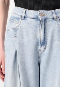 Lichtblauwe denimbroek met een hoge taille, een platte voorkant en diepe zakken; heeft contrasterende stiksels en een enkele knoopsluiting.