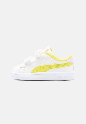 Pantof sport alb, tip low-top, cu dunguță galbenă, două barete velcro și detaliu roz la călcâi, pe un fundal simplu deschis.