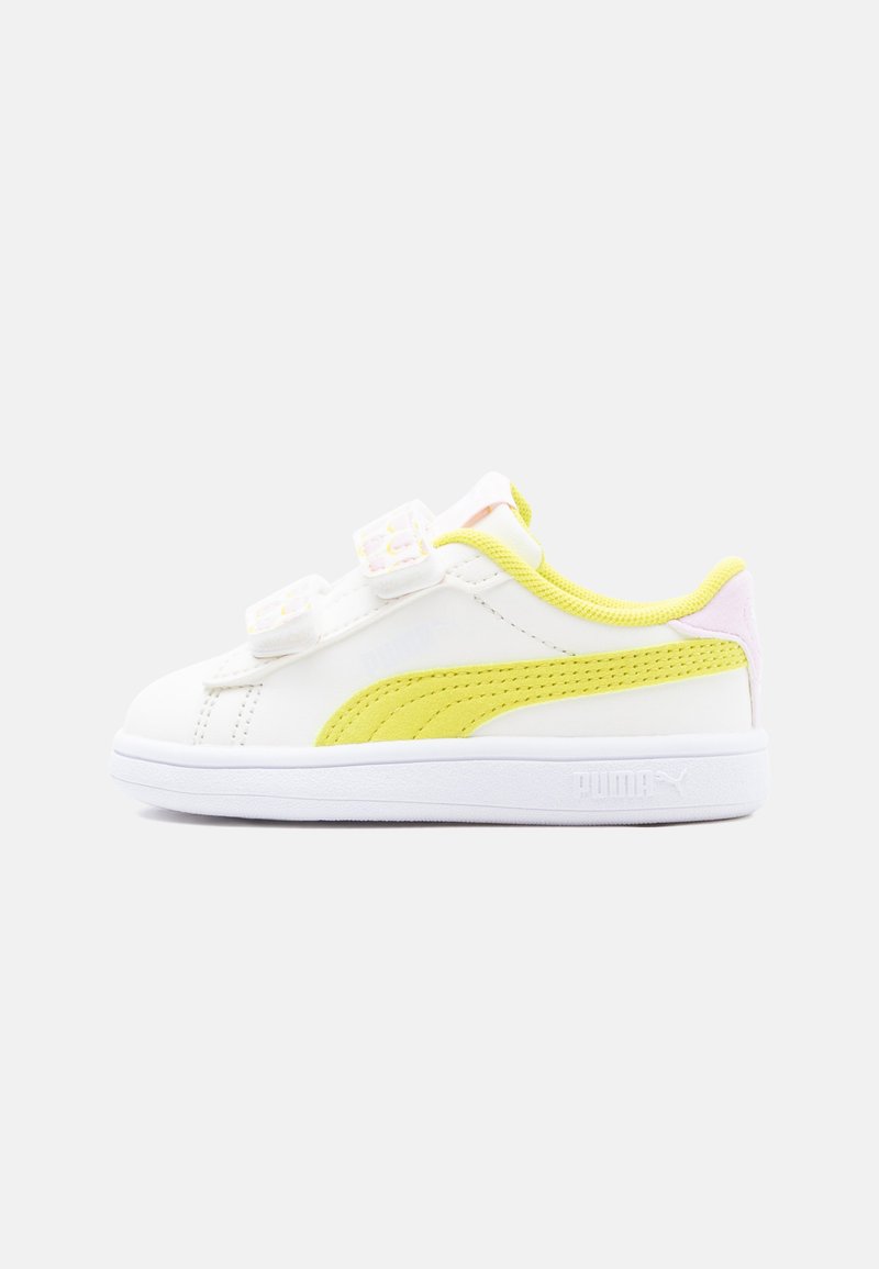 Weißer Sneaker mit niedrigem Schaft, gelbem Streifen, zwei Klettverschlüssen und pinker Fersendetail auf hellem einfarbigem Hintergrund.