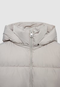 Beige gepolsterte Jacke mit hohem Kragen, ausgestattet mit einem Reißverschluss auf der Vorderseite und einer glatten, glänzenden Textur. Der Stoff scheint leicht und isoliert zu sein.