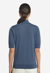 Kortärmad polo i blått tyg, strukturerat med en slät yta. Har en platt krage, ribbade ärmslut och en rak fåll vid midjan.