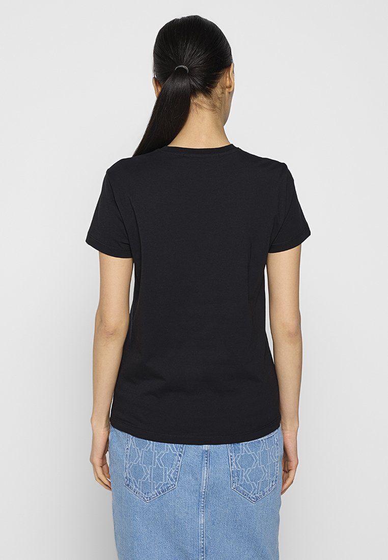 Schwarzes Baumwoll-T-Shirt mit kurzen Ärmeln und rundem Halsausschnitt. Getragen zu einem hellblauen Jeansrock mit sichtbaren Gesäßtaschen und einem Logomuster.