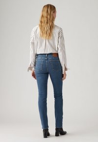 Blå denim skinny jeans med hög midja, bakfickor och ankellång design, kombinerat med en randig långärmad skjorta.