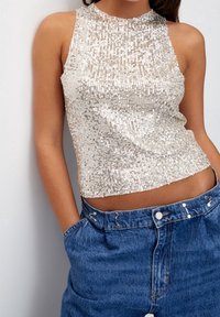 Zilver sequined mouwloos top met een hoge halslijn, gecombineerd met hoog-getailleerde blauwe denim shorts met drukknoopsluitingen.