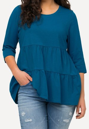 Top w kolorze morskim z rękawem do trzy czwarte, z wielowarstwowym wzorem, luźnym krojem i miękką fakturą. W zestawieniu z jasnoniebieskimi, postarzanymi dżinsami.