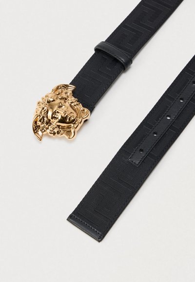 Μαύρη υφασμάτινη ζώνη με αγκράφα από μεταλλικό στοιχείο σε χρυσό τόνο με σχέδιο κεφαλιού λιονταριού. Ο ιμάντας διαθέτει υφή με ανάγλυφο σχέδιο και ρυθμιζόμενες τρύπες.