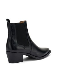 Botín de cuero negro hasta el tobillo con punta afilada, paneles laterales elásticos y un tacón bajo apilado. Textura suave con un sutil brillo.