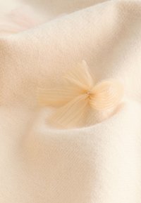 Tela suave de color crema con un delicado detalle de lazo de tul a juego que reposa sobre su superficie texturizada.