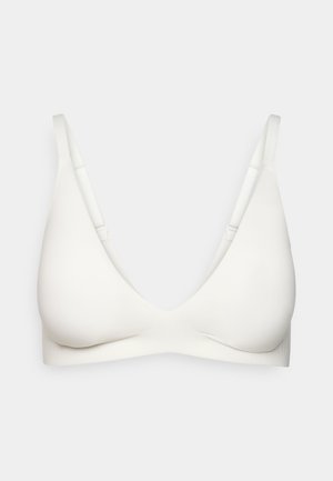 Hvit trådløs BH med justerbare skulderstropper og glatte, sømløse kopper på en enkel, lys bakgrunn.